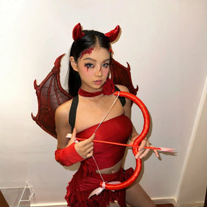 Adult evil cupid costume with red horns, demon wings, a red top, skirt, and a bow and arrow prop, featuring sheer gloves and flower accessory.