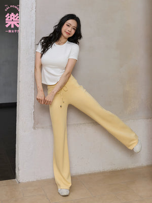 Model wearing yellow straight leg sweatpants with white top, seated side view