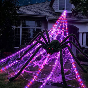 Halloween decorations featuring a large black furry spider with red eyes on an illuminated purple spider web structure outdoors at night.