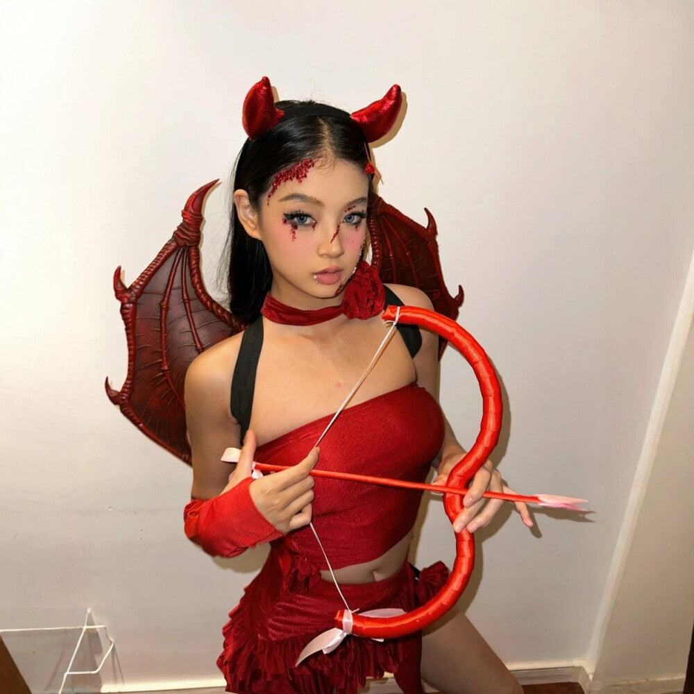 Adult evil cupid costume with red horns, demon wings, a red top, skirt, and a bow and arrow prop, featuring sheer gloves and flower accessory.