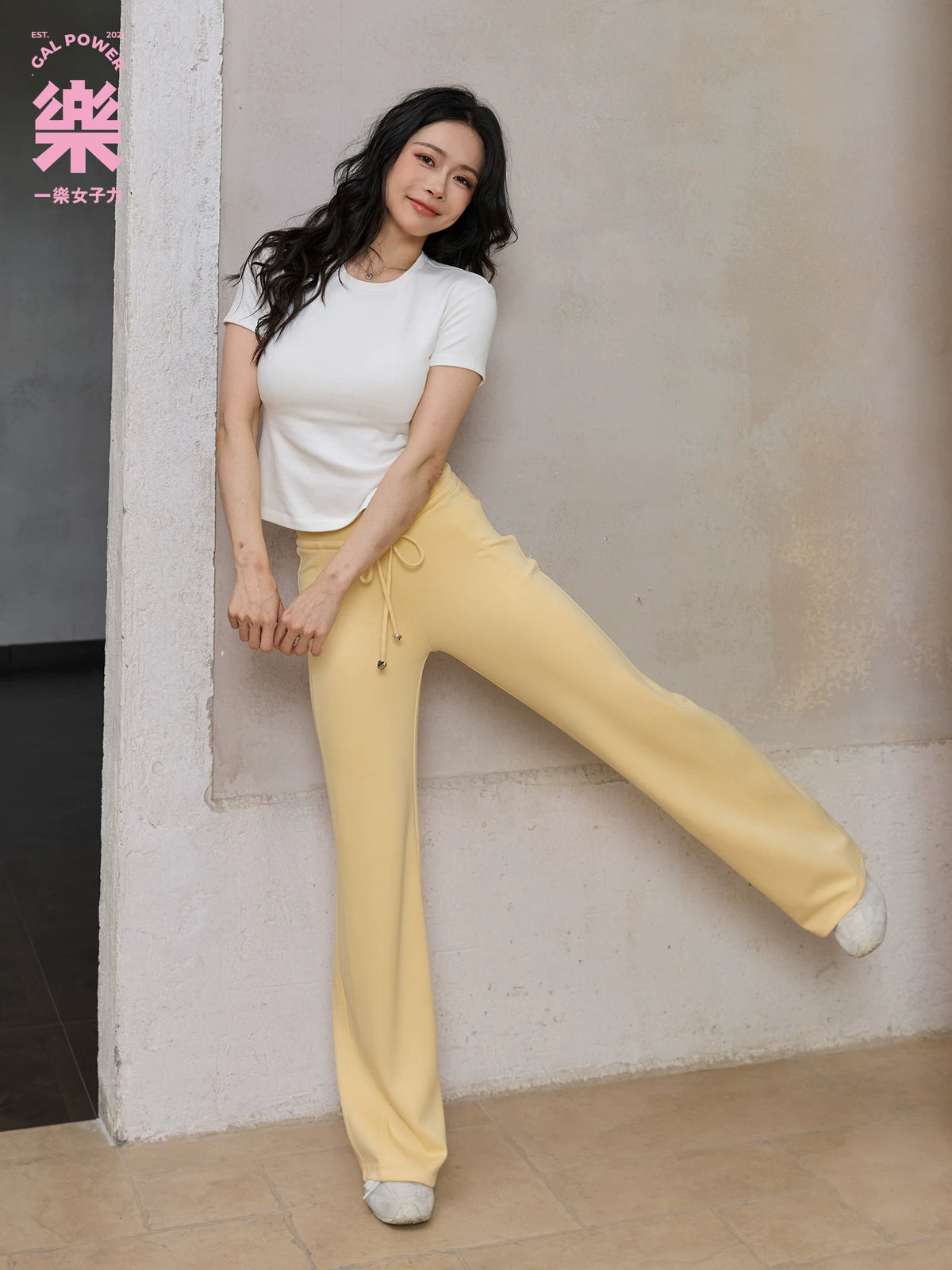 Model wearing yellow straight leg sweatpants with white top, seated side view