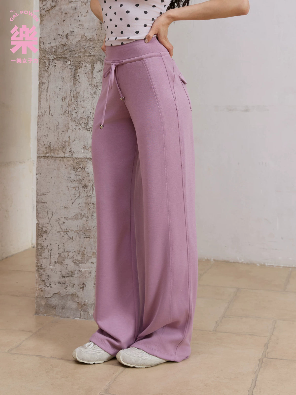 Model wearing purple straight leg sweatpants with polka dot top, side view