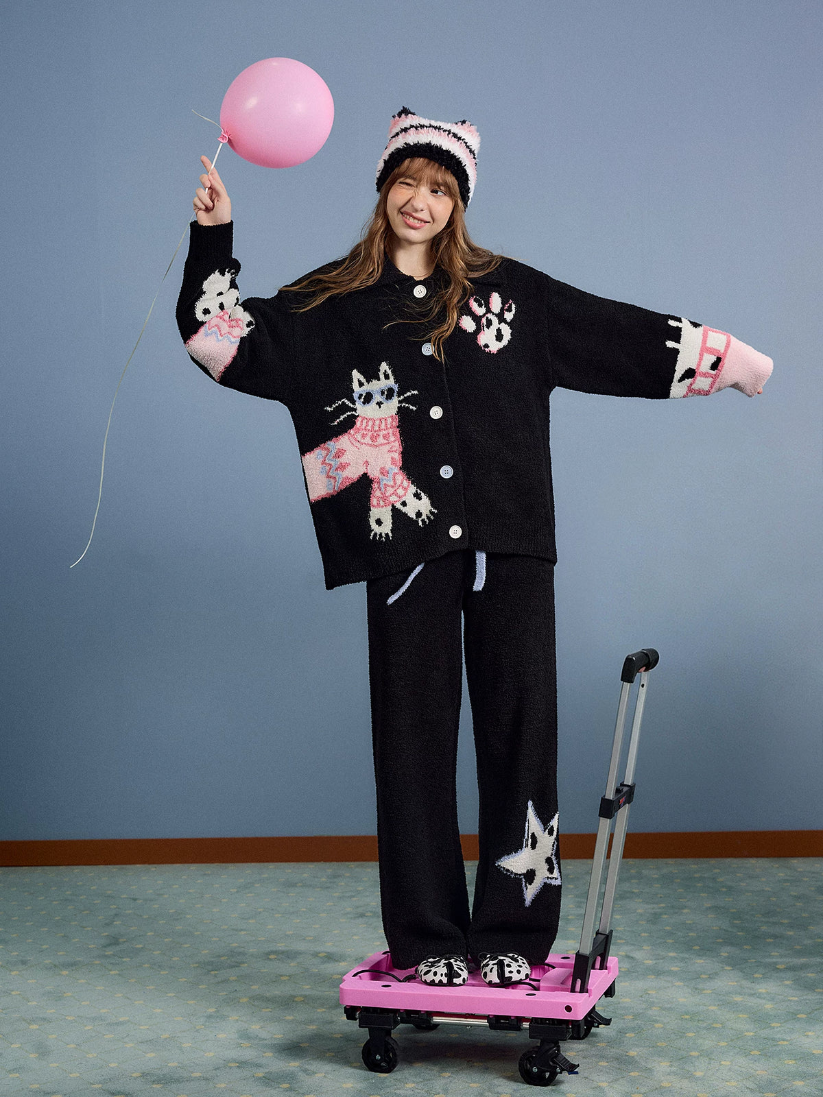 Model wearing the black fleece pajama set holding pink balloon, full body front view with arms out