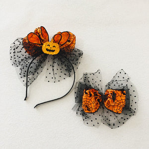 Halloween children's headband with black polka dot tulle, orange spider web patterned bows, and a glittery pumpkin face centerpiece.