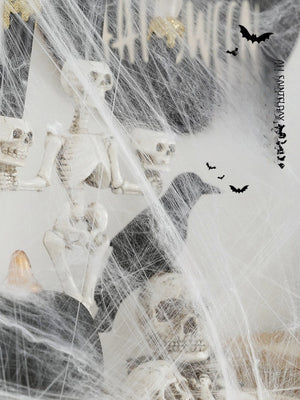 Halloween decorations featuring white synthetic spider webs, plastic skeletons, and skulls arranged in a spooky haunted house scene.