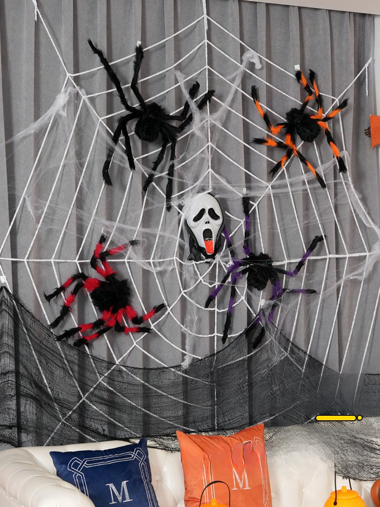 Halloween decorations featuring large colorful fuzzy spiders on a white spider web with a ghost face mask in the center on a gray background.